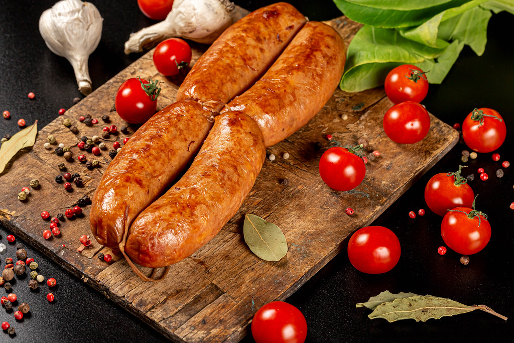 Sausages on a wooden board with tomatoes and seasoning